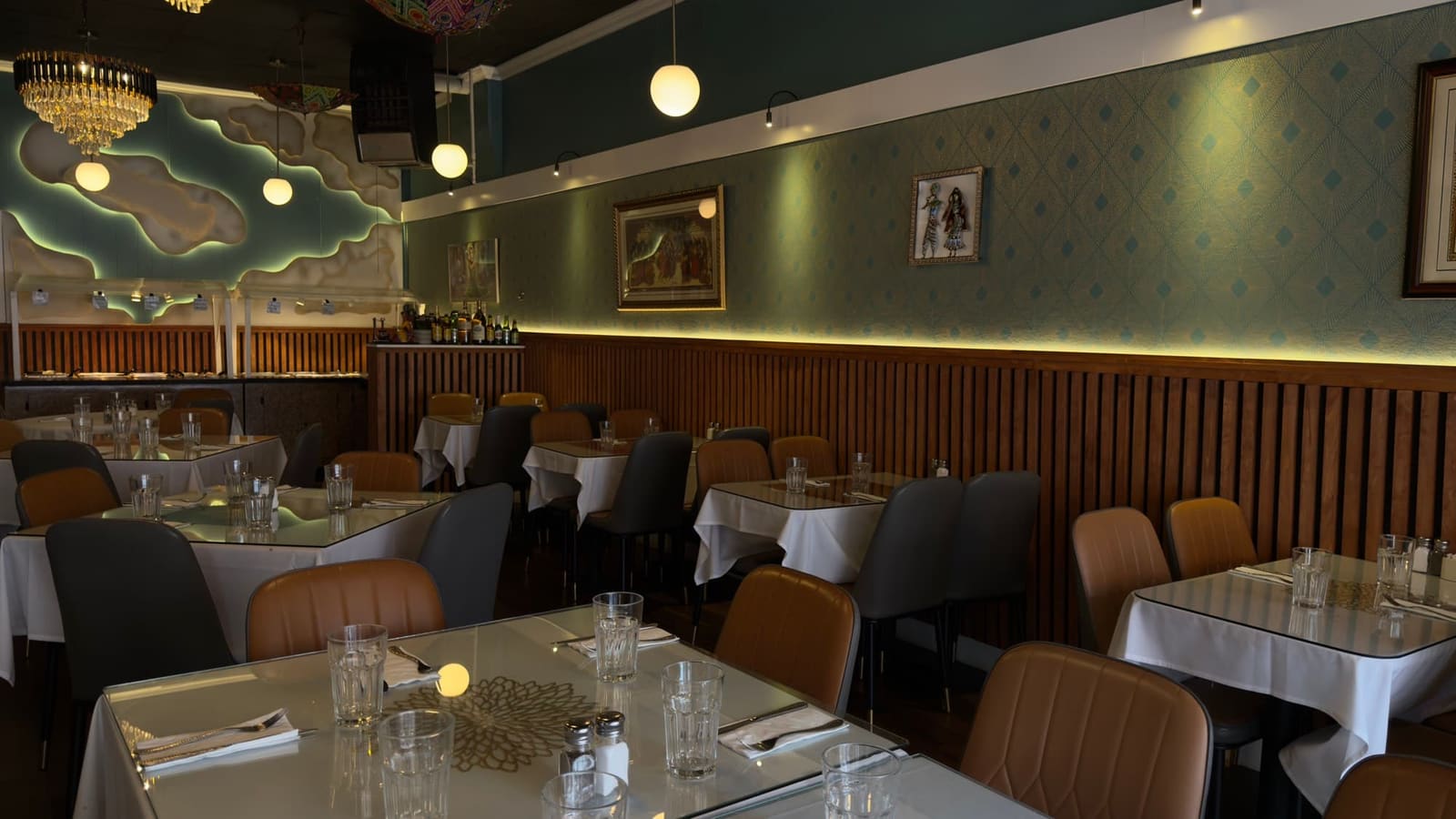 Interior dining room at Jewel of India in Seattle's University District, with chandeliers, patterned green walls, and set tables